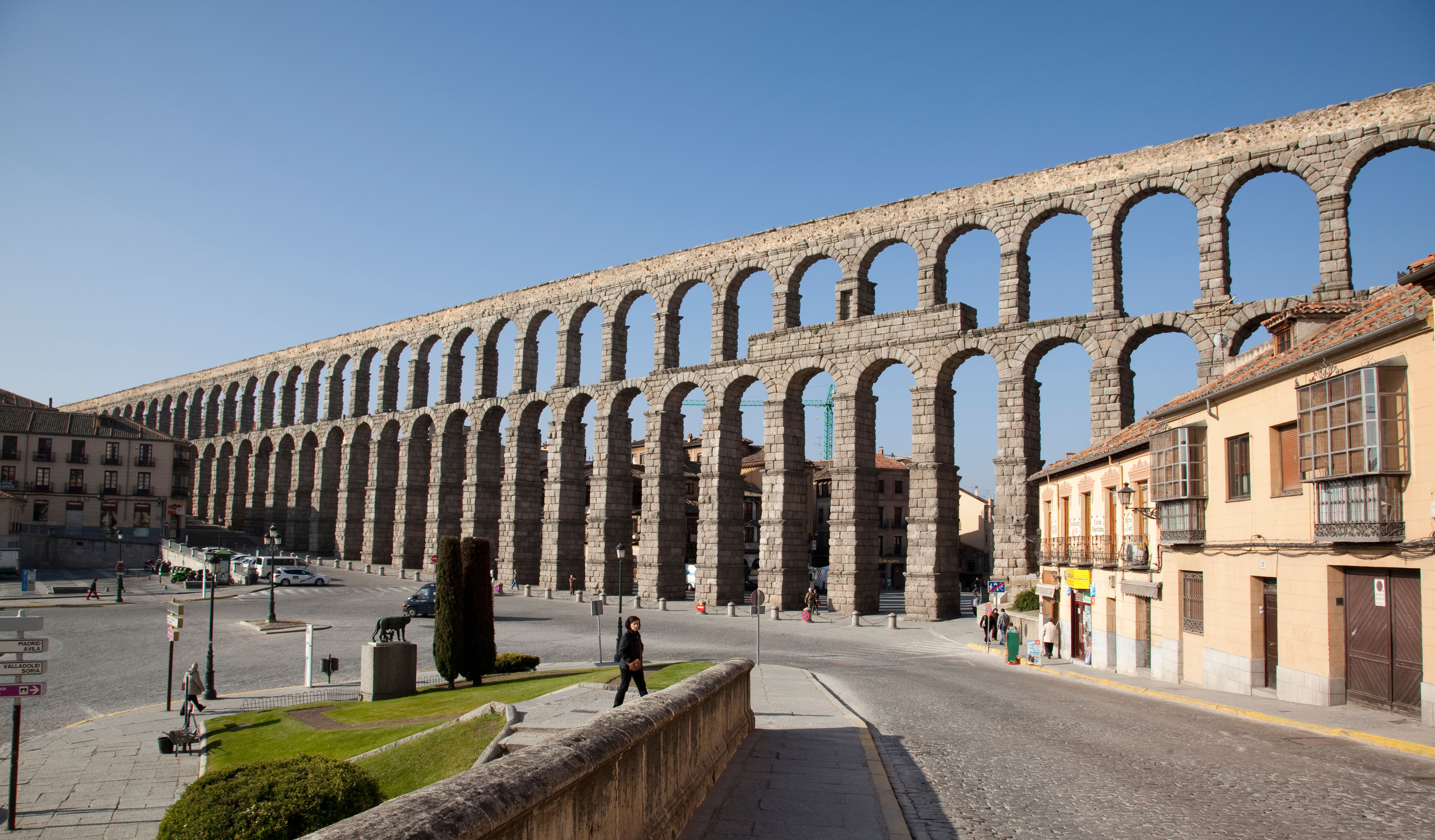 A towering aqueduct with two layers of arches stands in the centre of a modern town.
