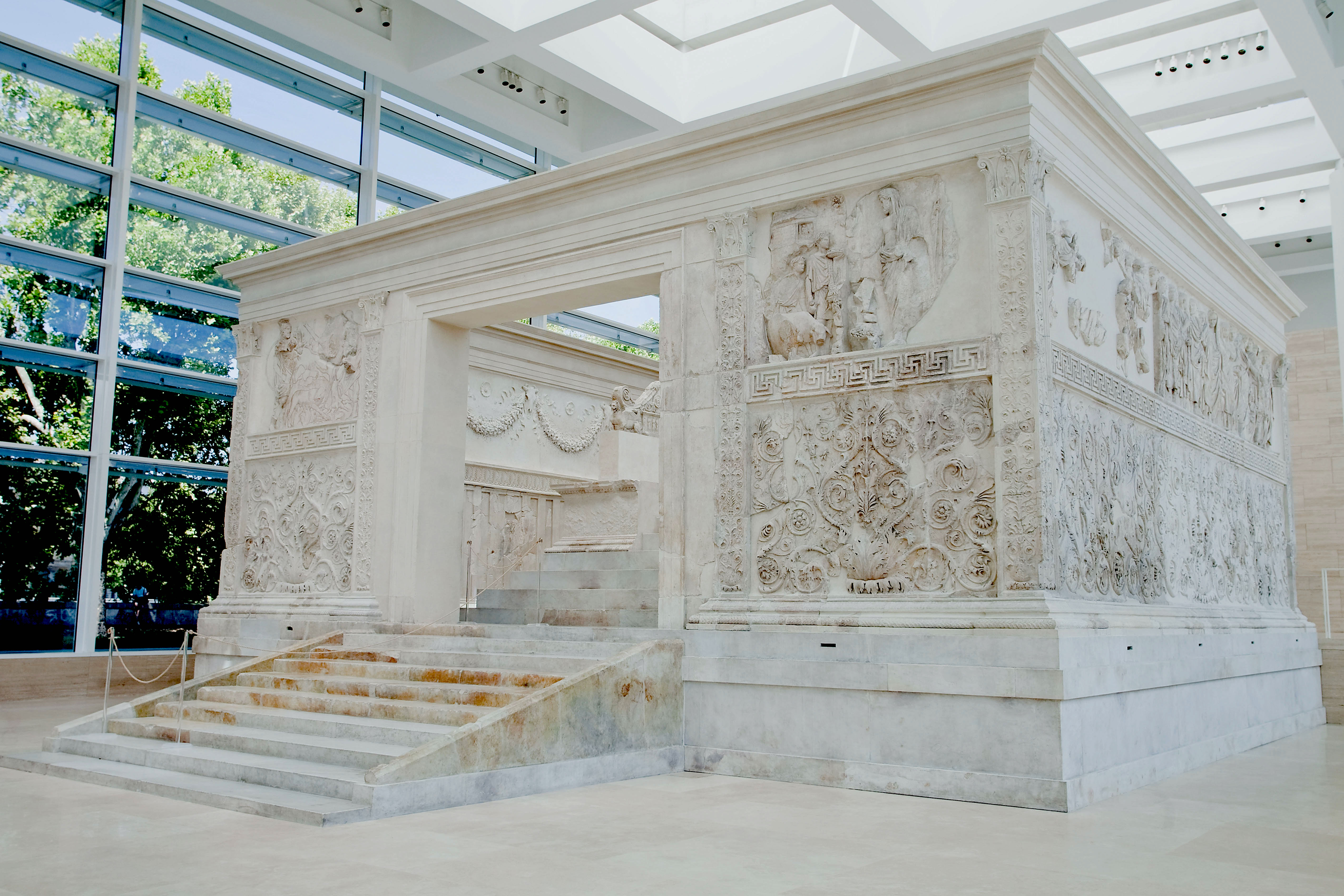 A large white stone monument with carvings on the walls. One side has an opening and stairrs goign up to the inside.